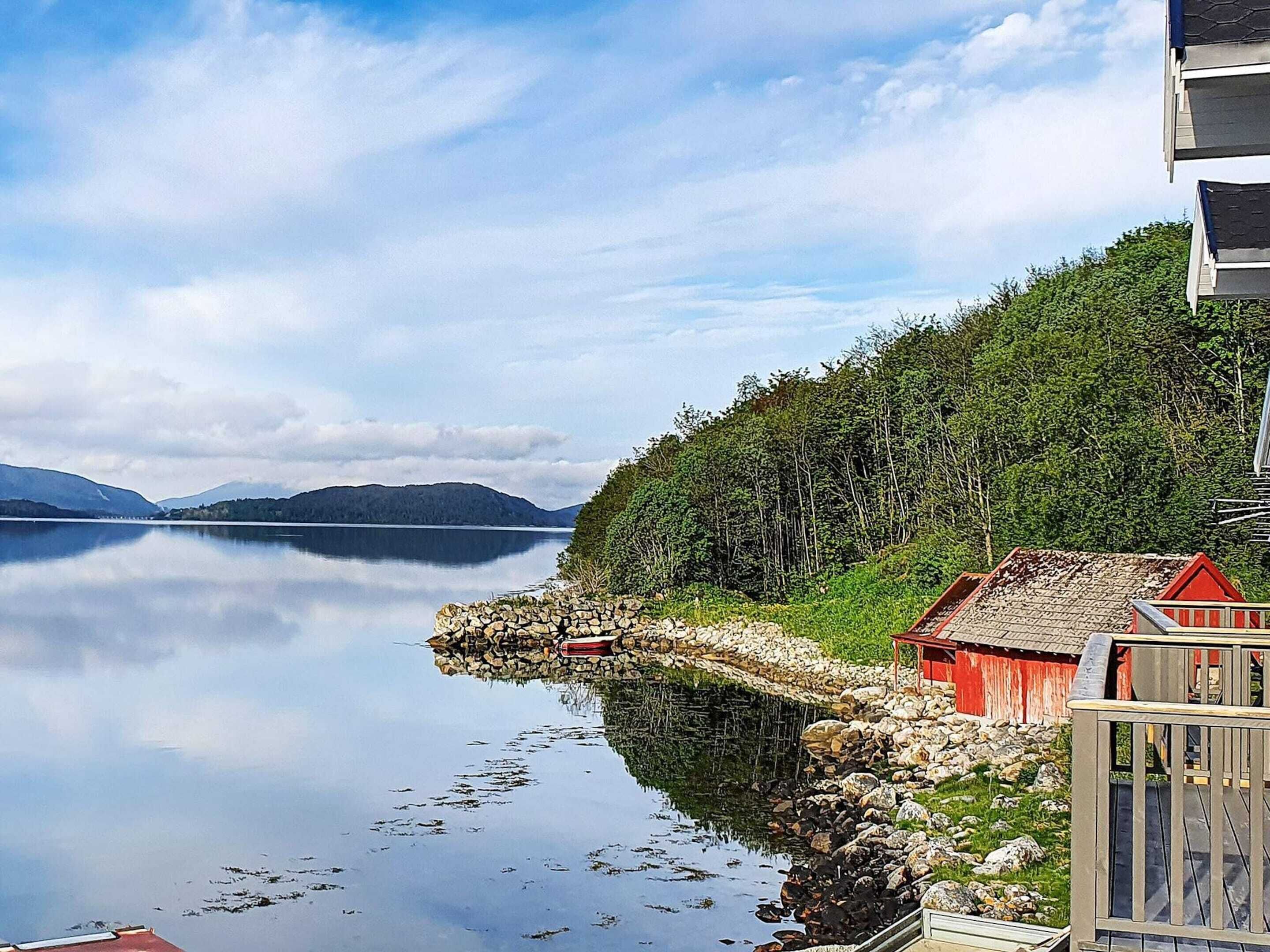 A calm lake with a stone pier, a red building, and a forested hillside.