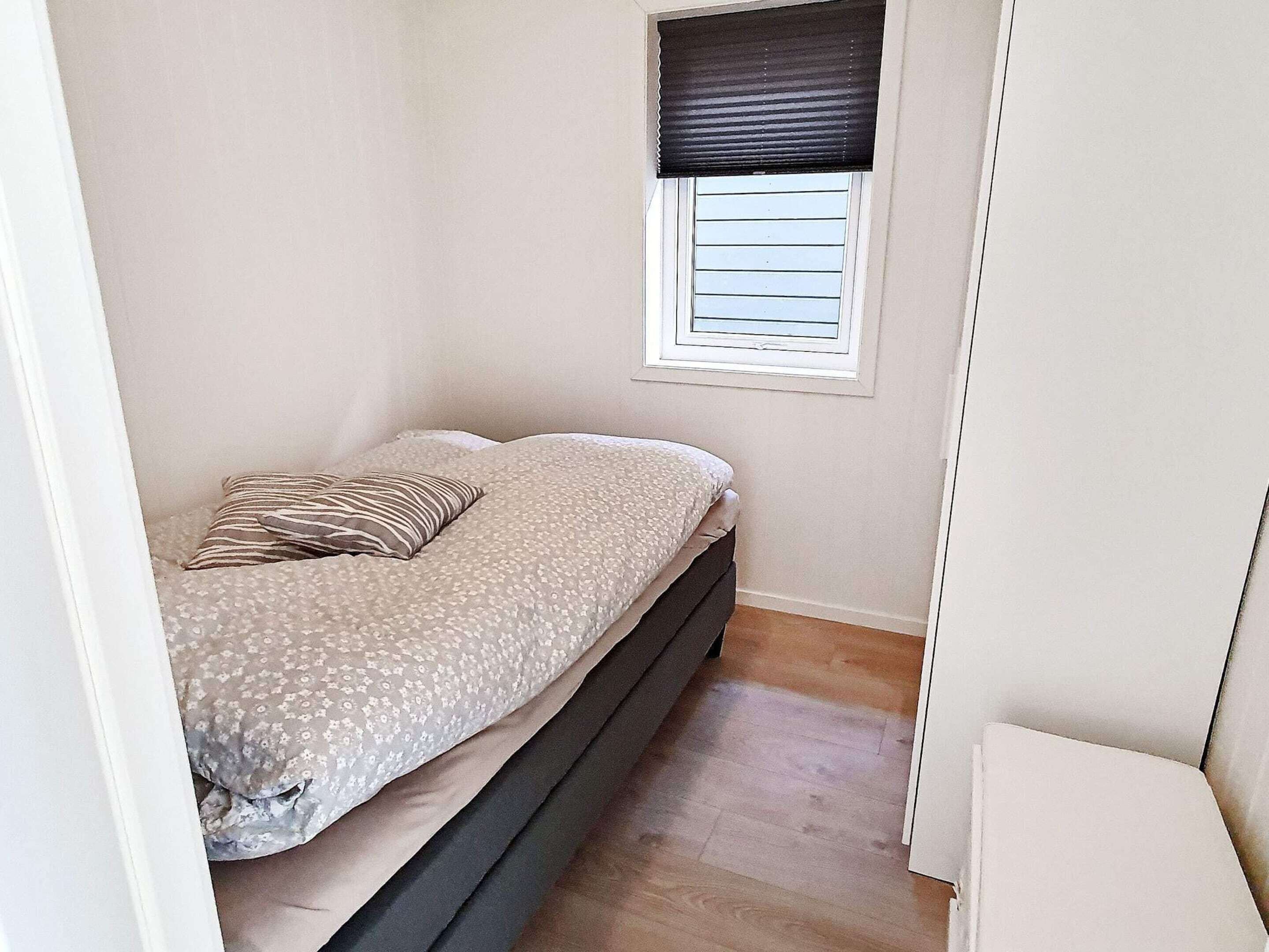 A small bedroom with a bed, a window with blinds, and a wooden floor.