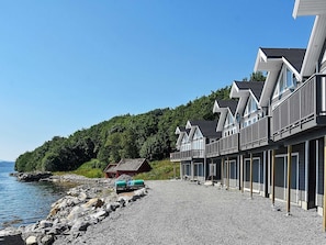 Uma fileira de cabanas à beira-mar com varandas, um caminho de cascalho e um pequeno galpão próximo à água.
