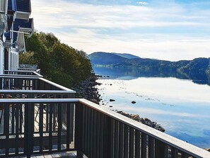 Una propiedad frente al lago con una terraza de madera que da a un lago tranquilo, rodeada de montañas.