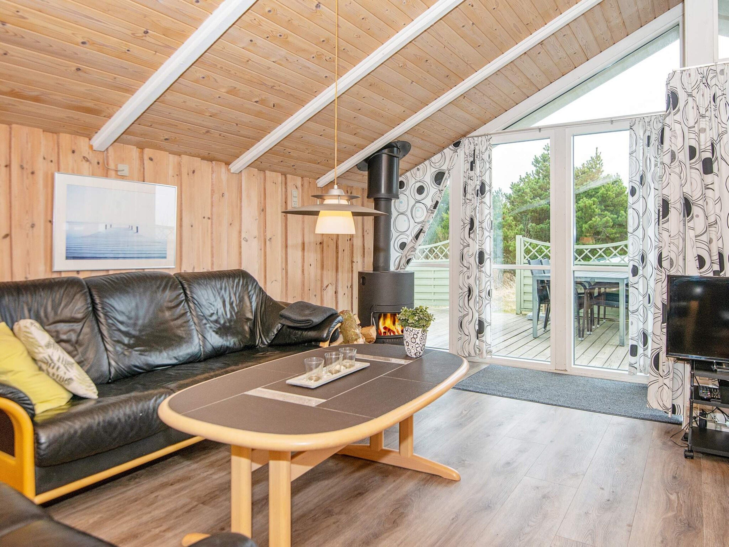 A cozy living room with a wooden ceiling, a black leather sofa, a wooden coffee table, and a fireplace.