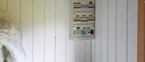 A room with white paneled walls, a white floor, and a wall-mounted electrical panel.