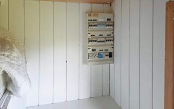 A room with white paneled walls, a white floor, and a wall-mounted electrical panel.
