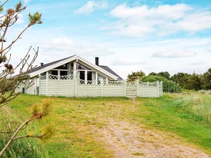 A single-story house with a sloped roof, a fenced yard, and a gravel path leading to the entrance.
