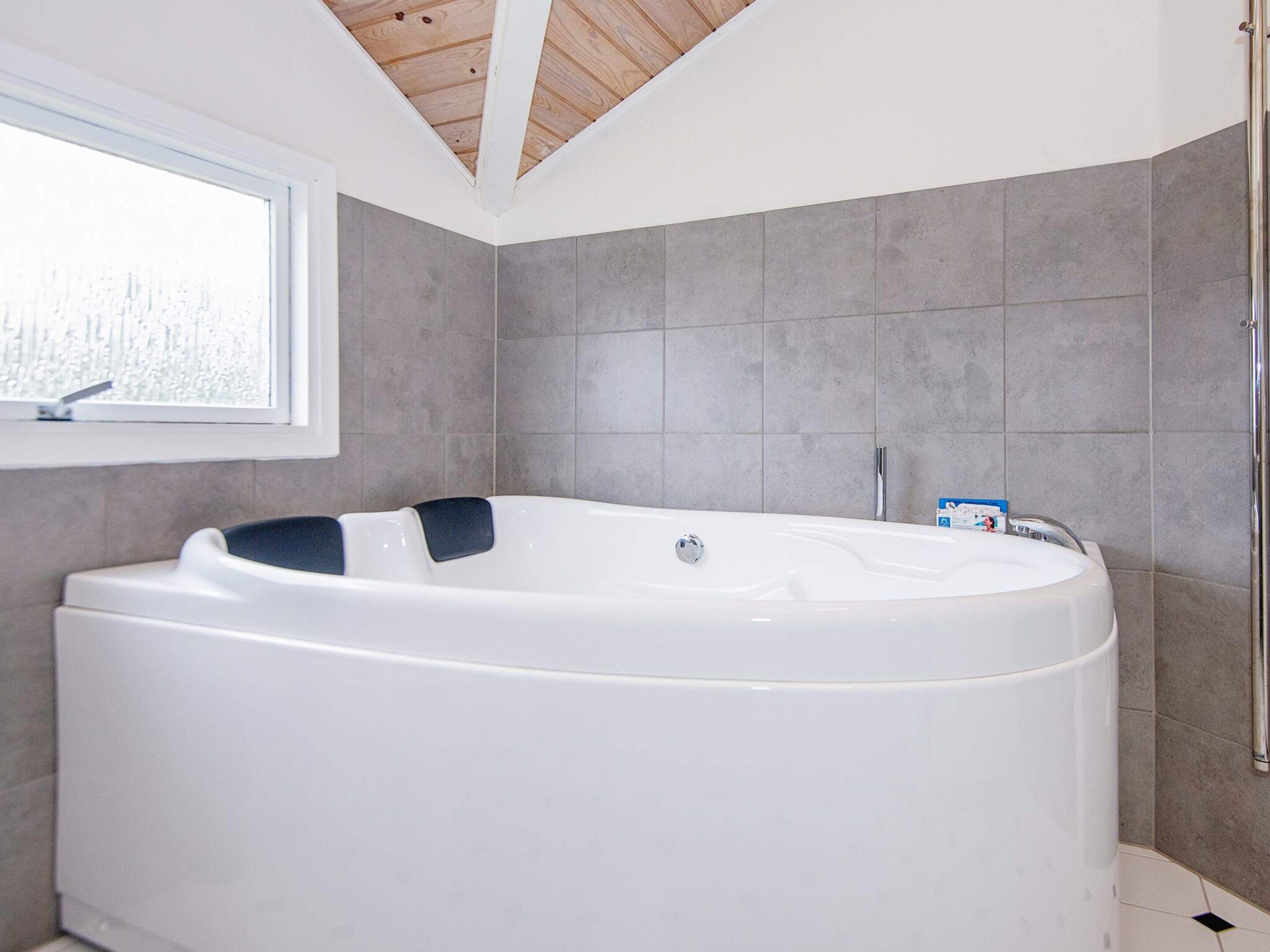 A modern bathroom with a freestanding bathtub, a window, and grey tiled walls.