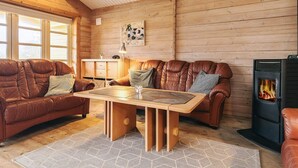 Een gezellig houten blokhutinterieur met houten plafond, een open haard, een zithoek en een eettafel.