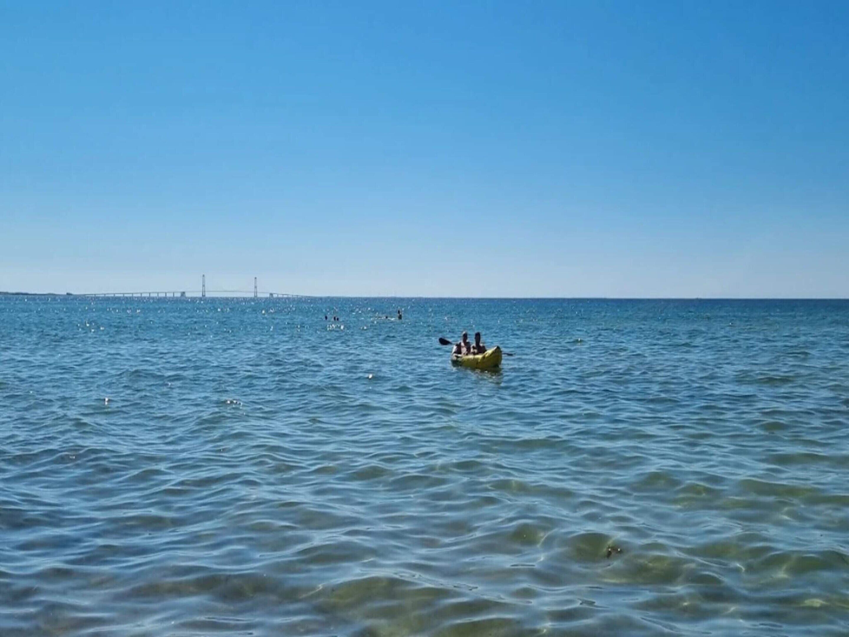 A calm sea with a bridge in the distance and a kayak with two people in the foreground.