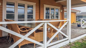 Een houten huis met een veranda, witte leuningen en rieten meubels.