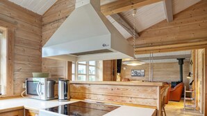 Het interieur van een houten hutje met een keukenhoek, inclusief een fornuis, magnetron en waterkoker.