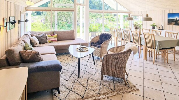 A spacious living area with a sofa, chairs, a dining table, and large windows offering a view of greenery. - Luxury Retreat in Nr. Lyngby-by Traum (Lokken)