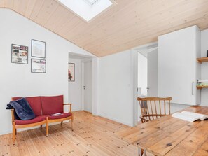 A modern living space with a wooden floor, a red sofa, a wooden dining table, and a skylight.