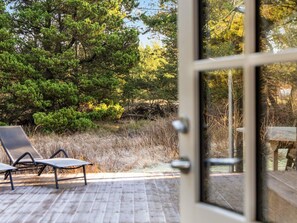 An outdoor deck with a lounge chair, surrounded by trees and a wooden fence.