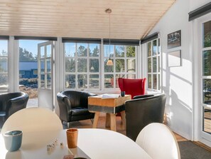 A room with a wooden ceiling, large windows, a table with chairs, and a red chair.