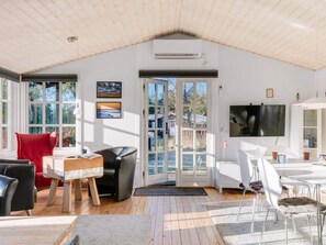 A spacious room with a high ceiling, large windows, a flat-screen TV, and a dining area with modern furniture.