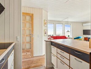 A modern kitchen with a wooden island, white cabinetry, and a red sofa in the adjacent living area. - Seaside Serenity at Vejlby Klit-by Traum (Glesborg)