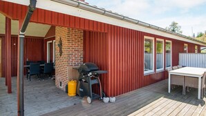 Een overdekt terras met een bakstenen schoorsteen, buitenmeubels, een barbecue en een tafel.