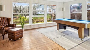 Een kamer met een pooltafel, een leren fauteuil en grote ramen met uitzicht op het omliggende landschap.