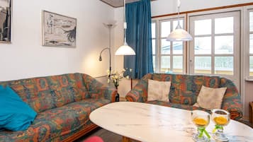 A room with two patterned sofas, a round table with two glasses, and a window with curtains.