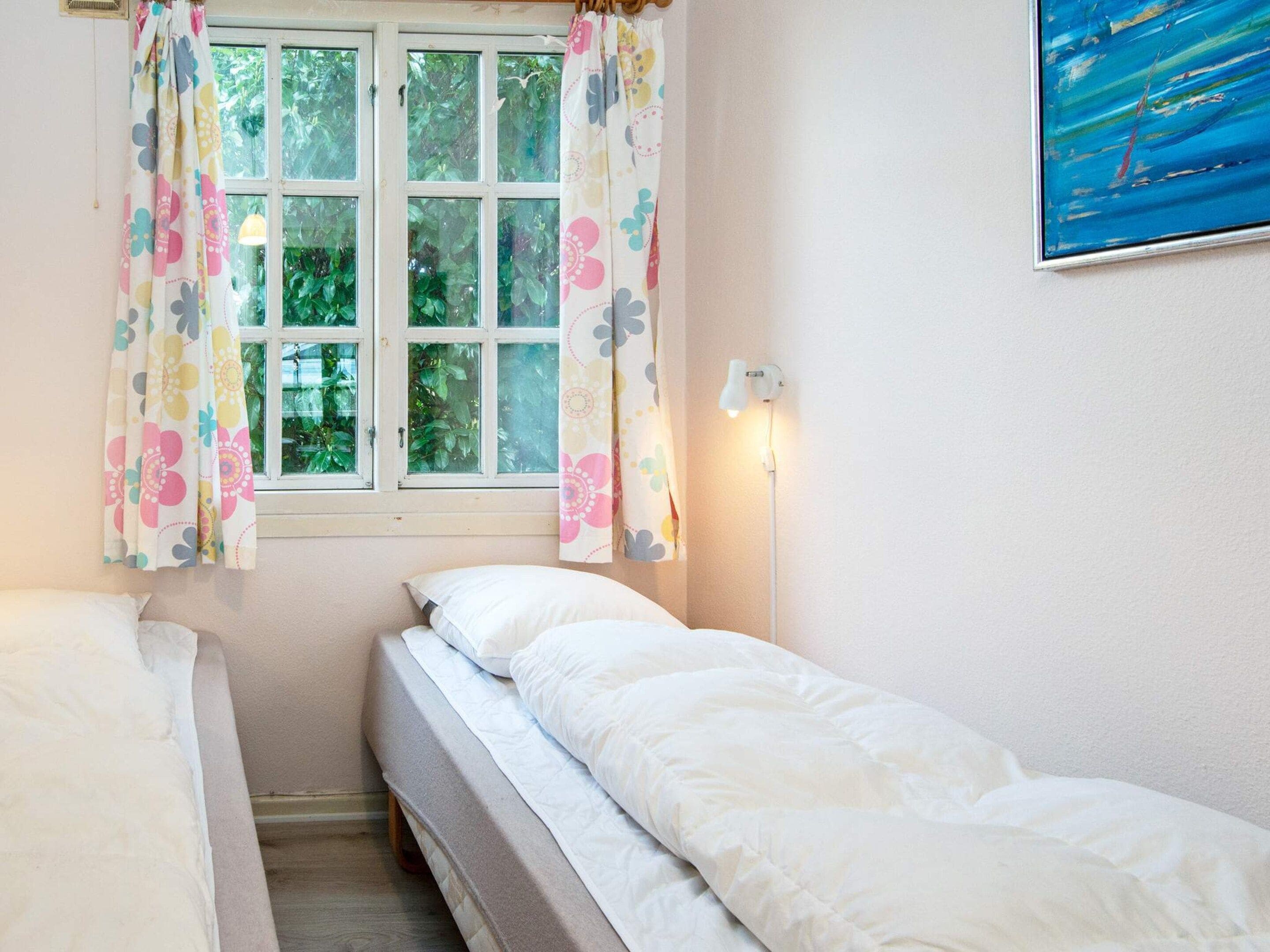Un dormitorio con dos camas, una ventana con cortinas, una lámpara de pared y un cuadro.