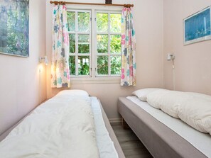 Une chambre avec deux lits, une fenêtre avec des rideaux, une lampe fixée au mur et un tableau.