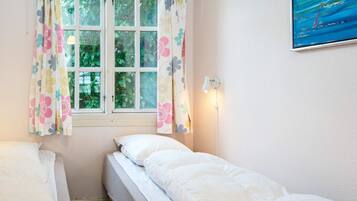 A bedroom with two beds, a window with curtains, a wall-mounted lamp, and a painting.
