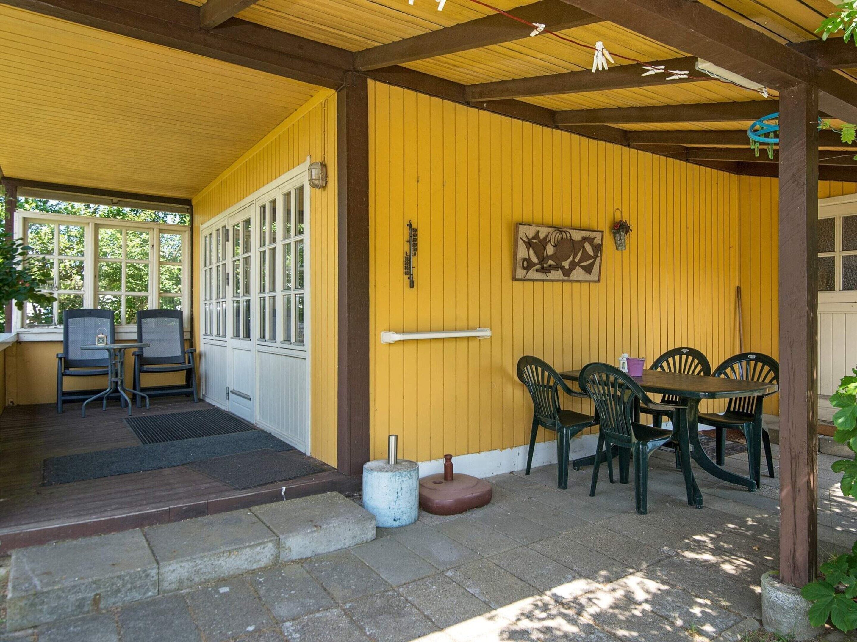 A covered patio area with a yellow wall, a table with chairs, and a door leading to an interior space.