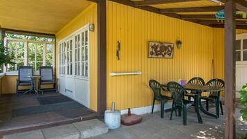 A covered patio area with a yellow wall, a table with chairs, and a door leading to an interior space.