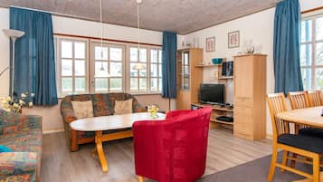 Et møbleret opholdsstue med sofa, en rød lænestol, spisebord med stole, fjernsyn og et skab.