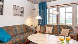 A room with two patterned sofas, a round table with two glasses, and a window with curtains.