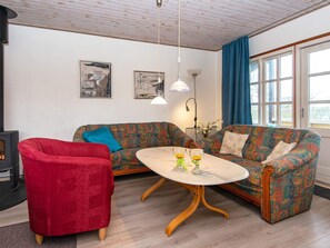 A living room with a sofa, a red armchair, a round coffee table, and a fireplace. - 4 Person Holiday Home in Nordborg (Nordborg)
