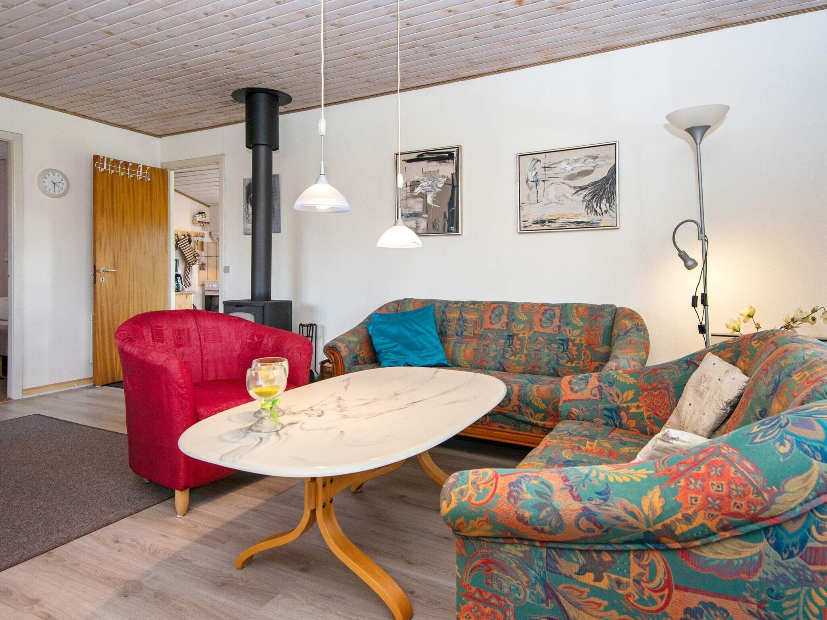 A cozy living room with a red armchair, a patterned sofa, a round table, and a black heater.