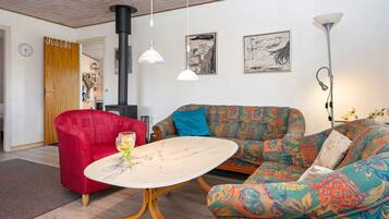 A cozy living room with a red armchair, a patterned sofa, a round table, and a black heater.