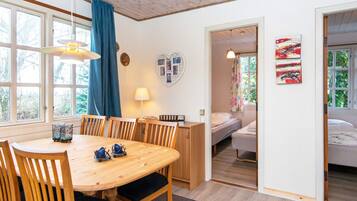 A room with a wooden dining table, chairs, a bed, and a window with curtains.