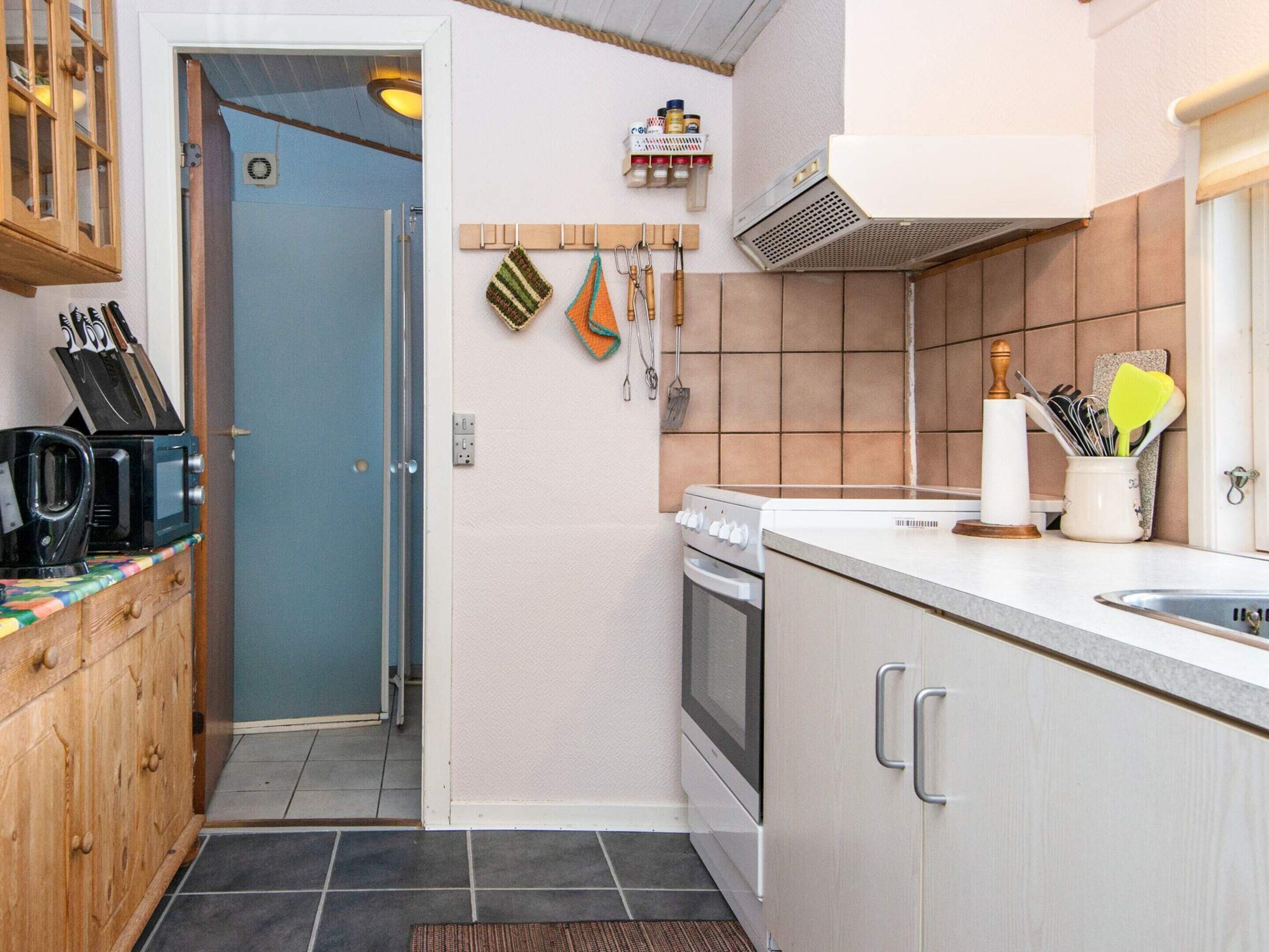 A compact kitchen with a microwave, stove, and sink. There is a wooden cabinet with a knife block and a small shelf with kitchen utensils.
