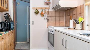A compact kitchen with a microwave, stove, and sink. There is a wooden cabinet with a knife block and a small shelf with kitchen utensils.