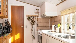 A kitchen with wooden cabinets, a stove, a sink, and a window with a view of trees.