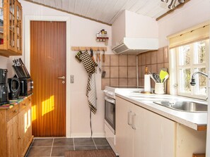 Une cuisine avec des meubles de rangement en bois, une cuisinière, un évier et une fenêtre donnant sur les arbres.