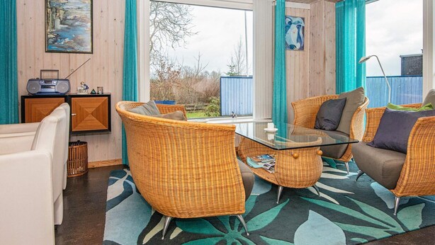 Une pièce chaleureuse, meublée de meubles en osier, avec une table en verre et une vue sur l’extérieur.