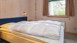 Une pièce aux murs lambrés, avec un lit, une fenêtre avec des rideaux et un luminaire fixé au mur.