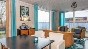 Une pièce chaleureuse avec un plafond en bois, une table à manger avec des chaises, un canapé en osier et une grande fenêtre avec des rideaux.