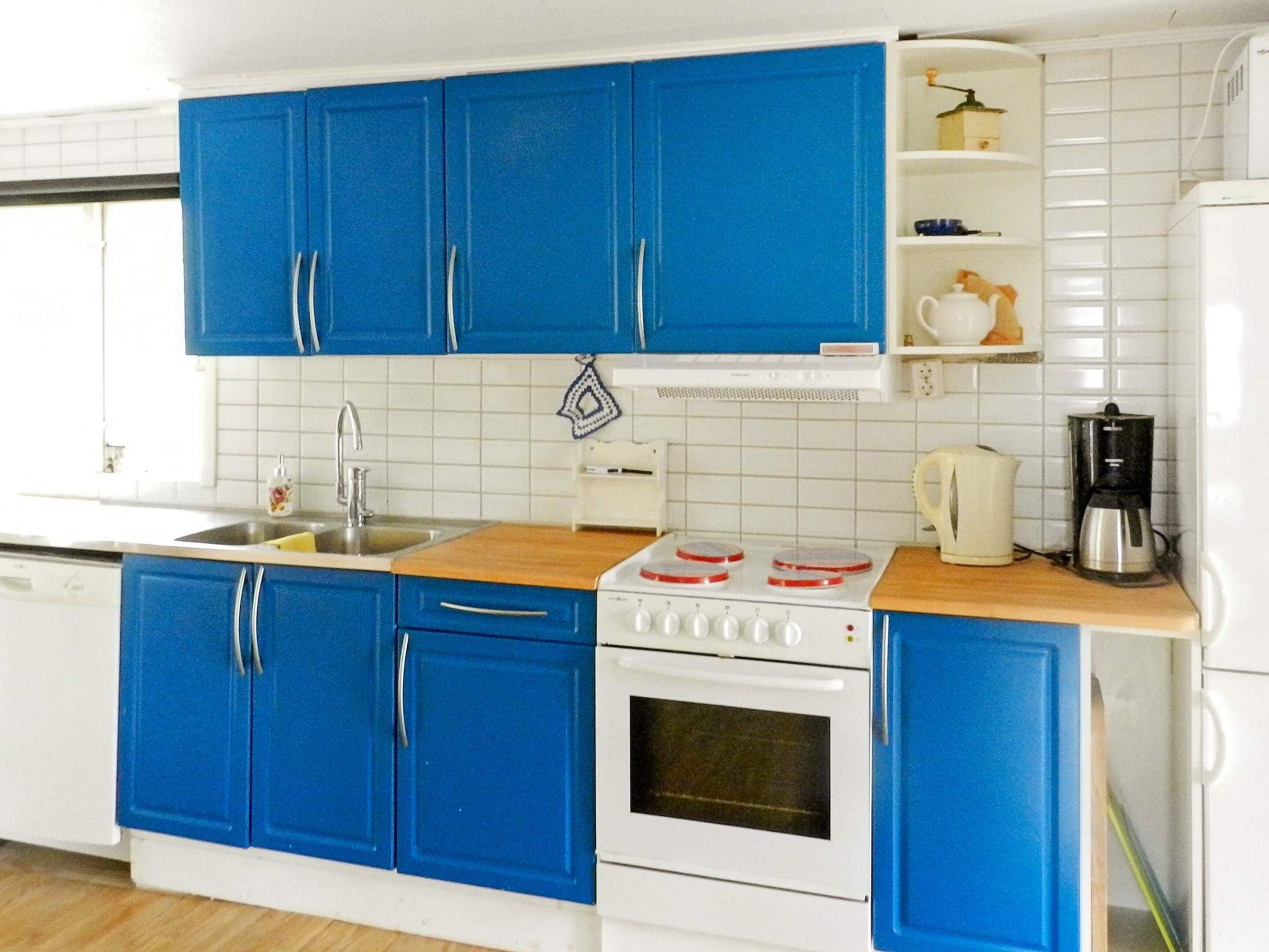 A kitchen with blue cabinets, a white stove, a sink, and a coffee maker.