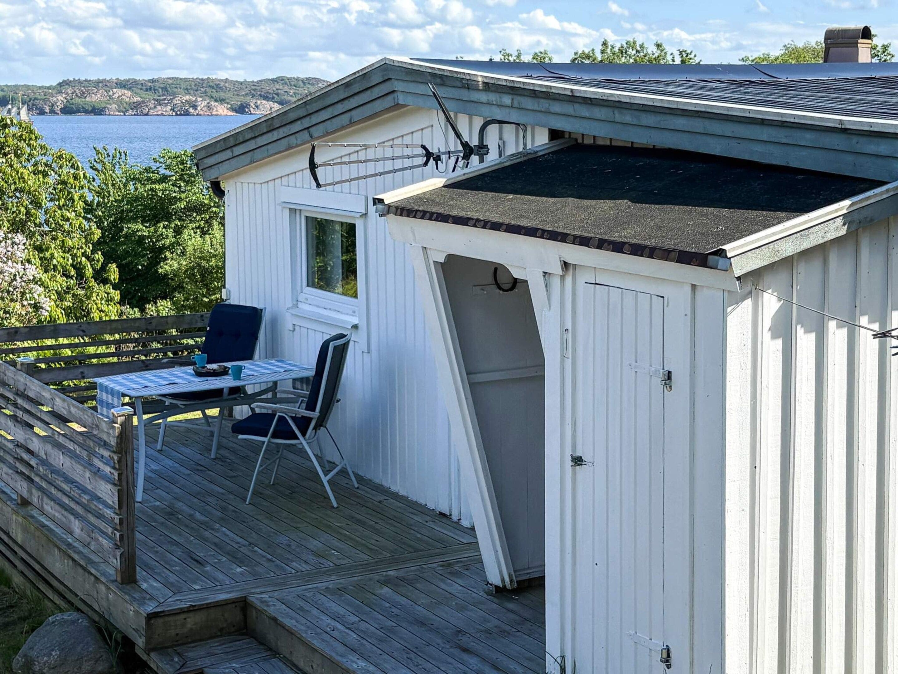 A white building with a deck, a table with chairs, and a view of the sea.
