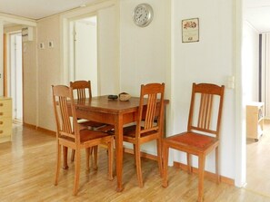 A dining area with a wooden table and four chairs, a wall clock, and a small floral decoration.