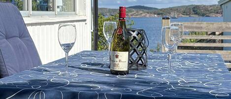 A table with a bottle of wine, two glasses, and a metal basket on a tablecloth with a coastal view.
