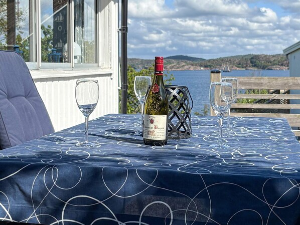 A table with a bottle of wine, two glasses, and a metal basket on a tablecloth with a coastal view. - 4 Star Holiday Home in Lysekil (Lysekil)