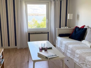 A room with a bed, a table with a book and glasses, a lamp, and a window with a view of trees and water.