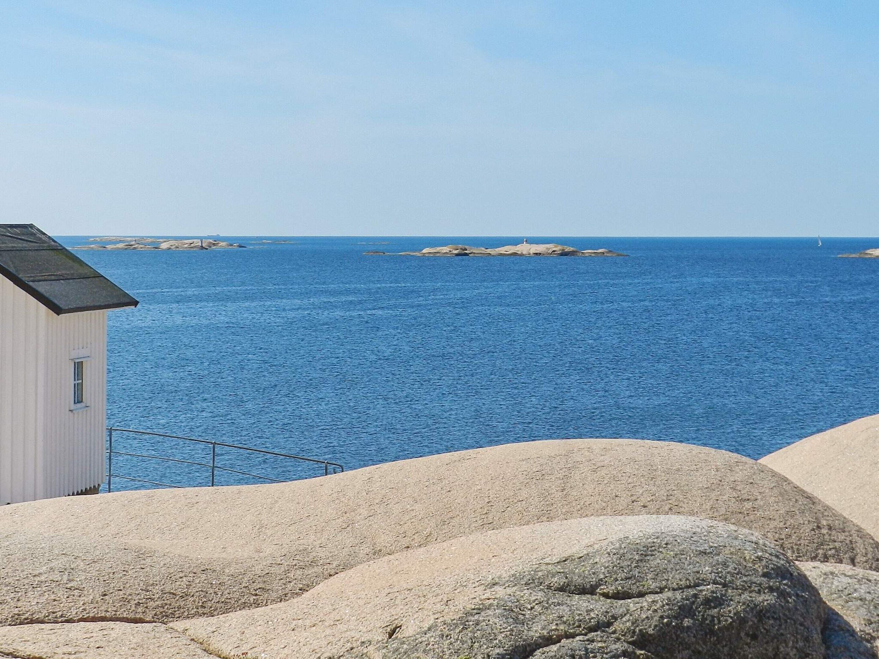 A coastal view with a white building, large rocks, and calm blue sea.