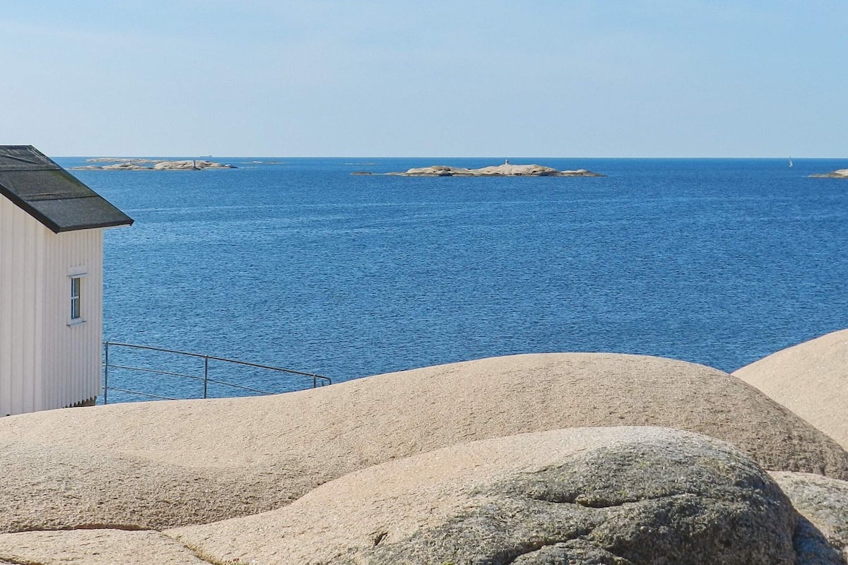 A coastal view with a white building, large rocks, and calm blue sea.