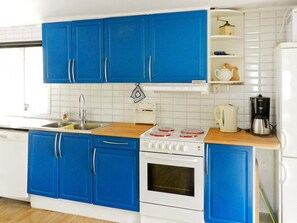 A kitchen with blue cabinets, a white stove, a sink, and a coffee maker. - 4 Star Holiday Home in Lysekil (Lysekil)