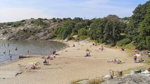 A beach with people sunbathing and swimming, surrounded by greenery and rocky terrain. - 4 Star Holiday Home in Lysekil (Lysekil)